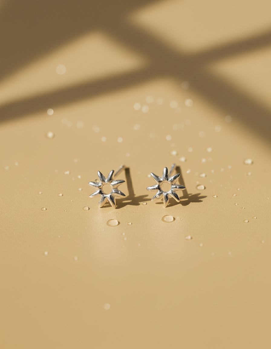 Silver star stud earrings photographed with soft sunlight and ocean water droplets, ocean-proof design